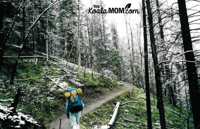 Woman hiking the Lake Minnewanka trail with snow falling.