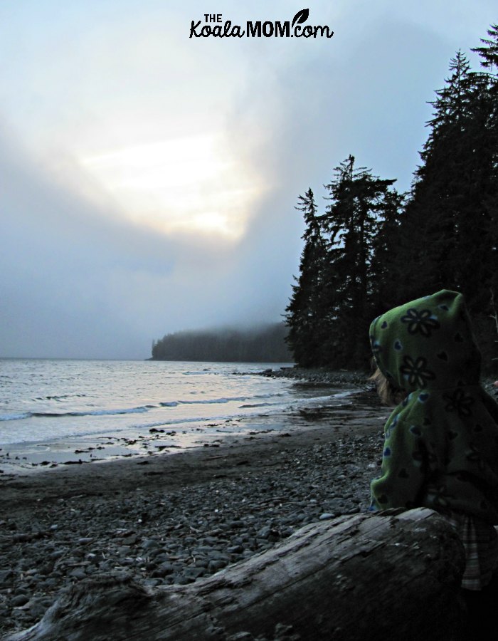 Toddler sitting on a log on China Beach, watching the sunset over the waves.