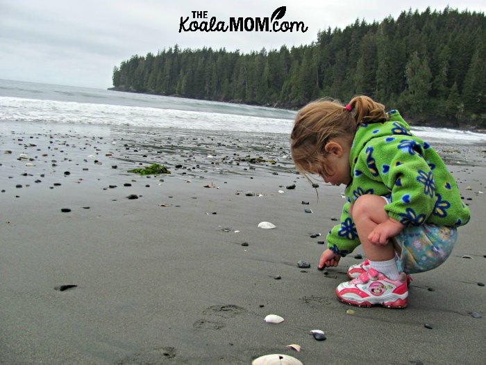 Toddler in bright clothes playing with rocks on a beach.