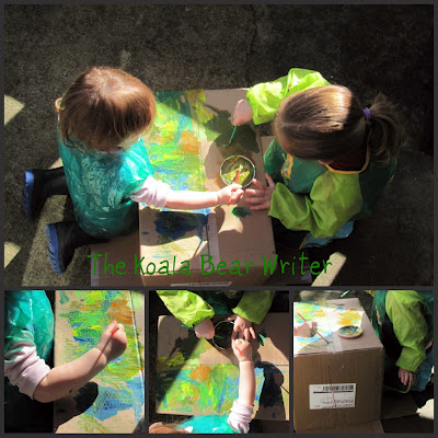 Two little girls painting outside on a box in green smocks.