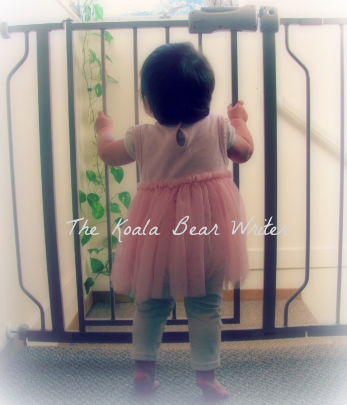 Baby girl standing at a baby safety gate