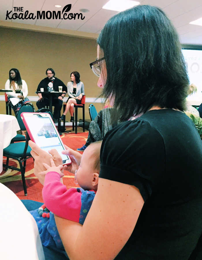 Mom taking notes at a conference on a tablet with baby on her lap.