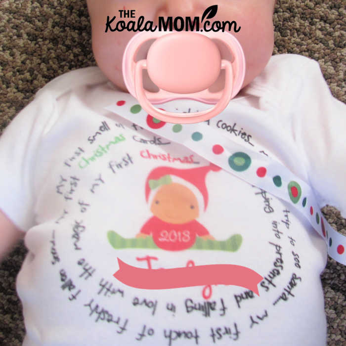 Baby wears her adorable Christmas onesie while sucking on a soother.