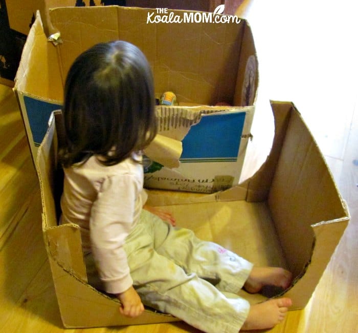 Toddler sitting in a simple cardboard box car.