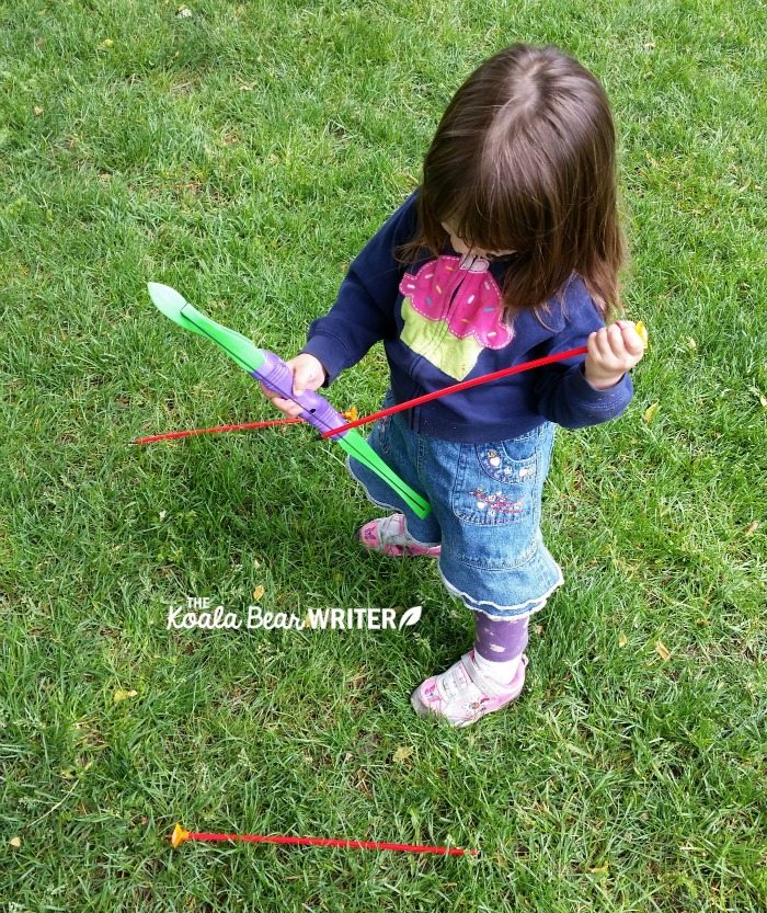 Toddler trying to figure out a toy bow and arrow.