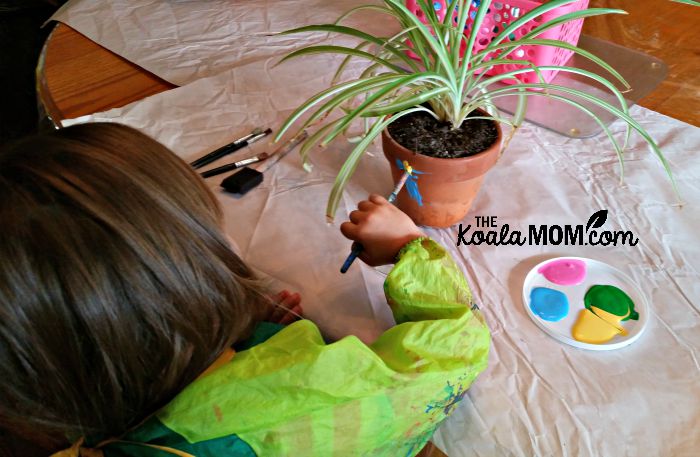 Lily painting her clay plant pot (with spider plant inside)