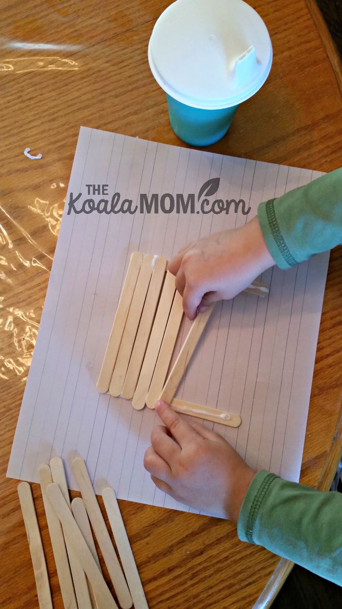 Toddler gluing craft sticks together to make a bird feeder