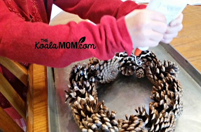 Sunshine putting glue on a pine cone wreath to decorate it