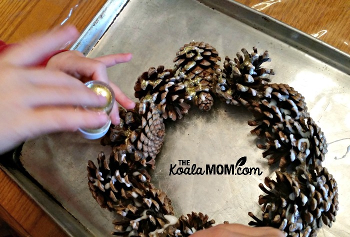 Applying glitter to a pine cone wreath