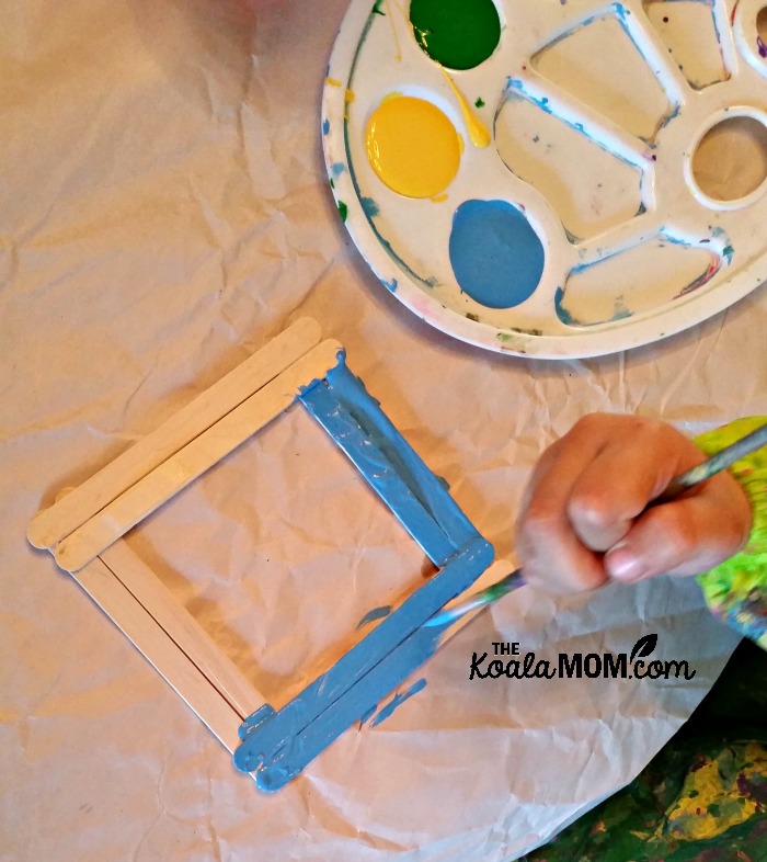 Toddler painting a craft stick picture frame