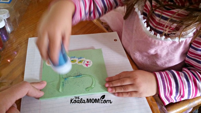 Toddler putting glitter on her notebook cover