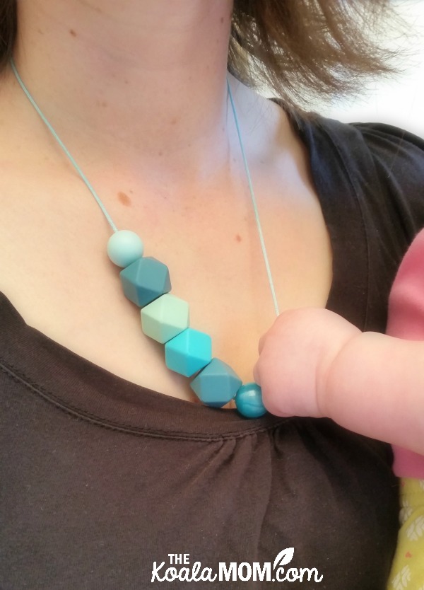 Baby holding a mom's teething necklace