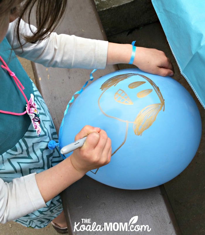 Lily drawing a face on her balloon at her 6th birthday party in the park.