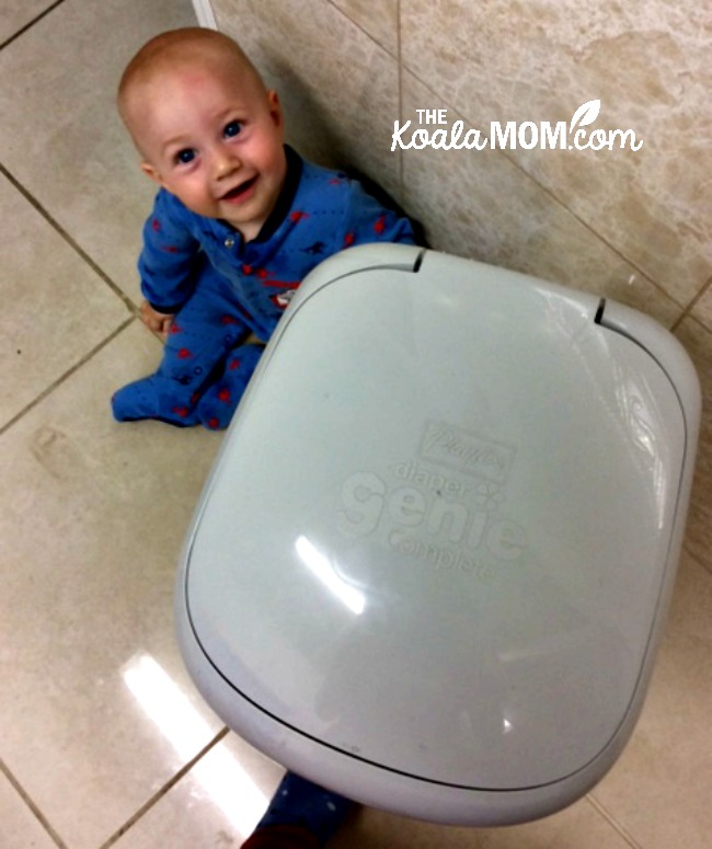 Happy baby sitting beside his Diaper Genie