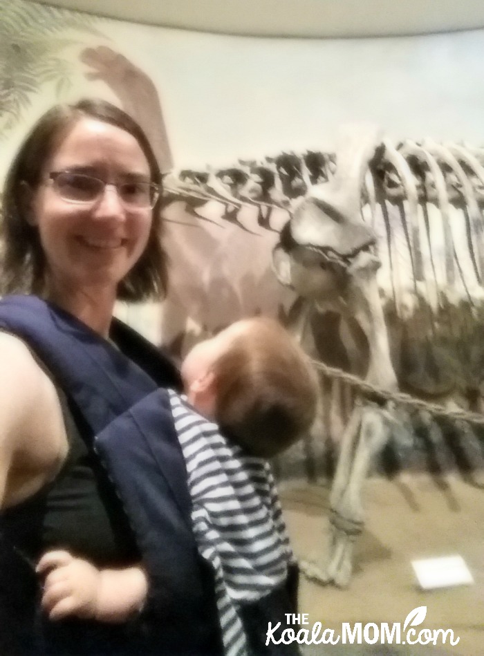 Baby-wearing mom with dinosaur skeleton at the Royal Tyrell Museum