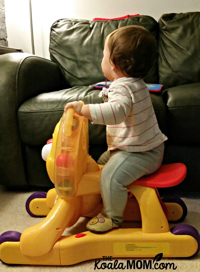 Baby sitting on a BrightStarts toy lion while wearing Kooshoo pants