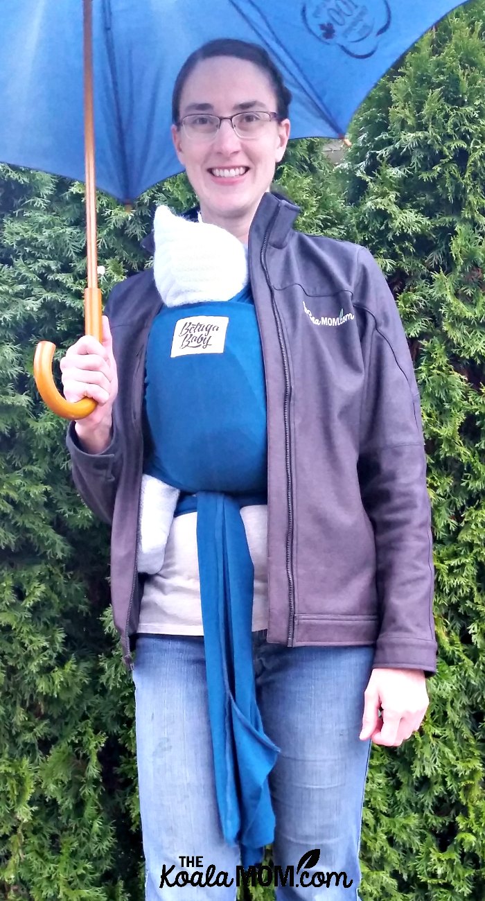 Mom wearing a baby in a Beluga Baby bamboo wrap carrier under her raincoat