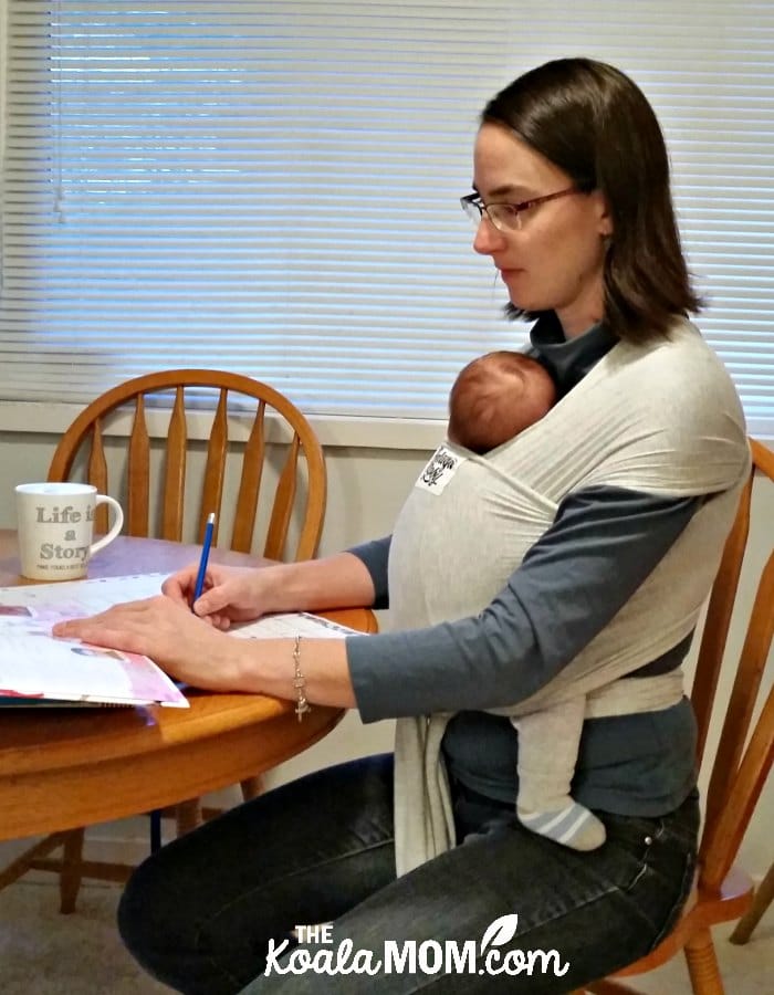 Homeschool mom going over lesson plans with baby wrapped in a Beluga Baby bamboo carrier.