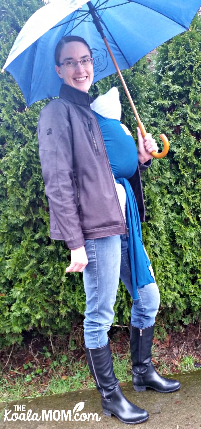 Mom wearing a baby in a Beluga Baby bamboo wrap carrier under her raincoat