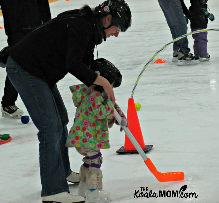 Pregnant mom helping her daughter skate with a hockey stick