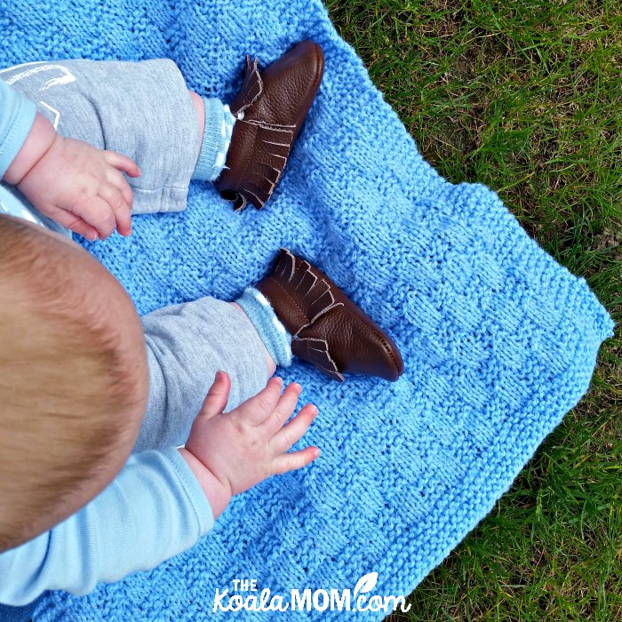 Baby sitting on a blanket wearing his brown fringed moccasins from Mia's Moccs