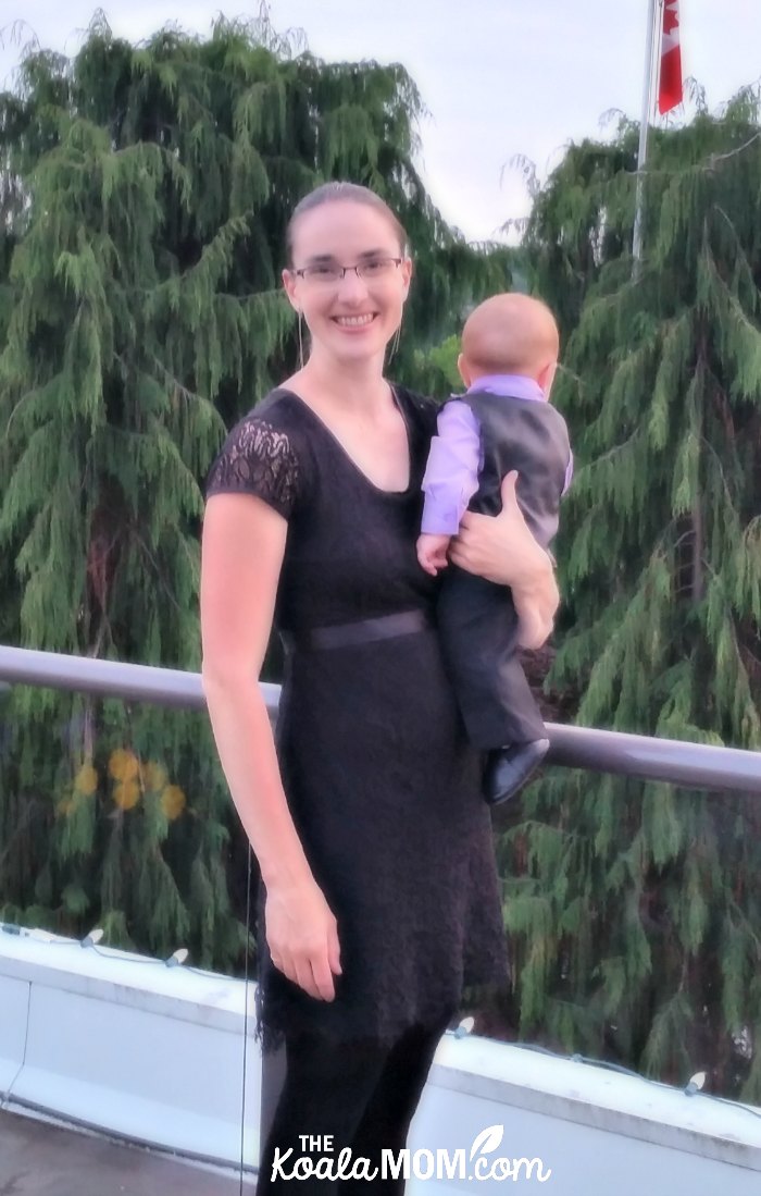 Breastfeeding mom wearing a Momzelle black lacy nursing dress and holding a baby in a black-and-purple suit