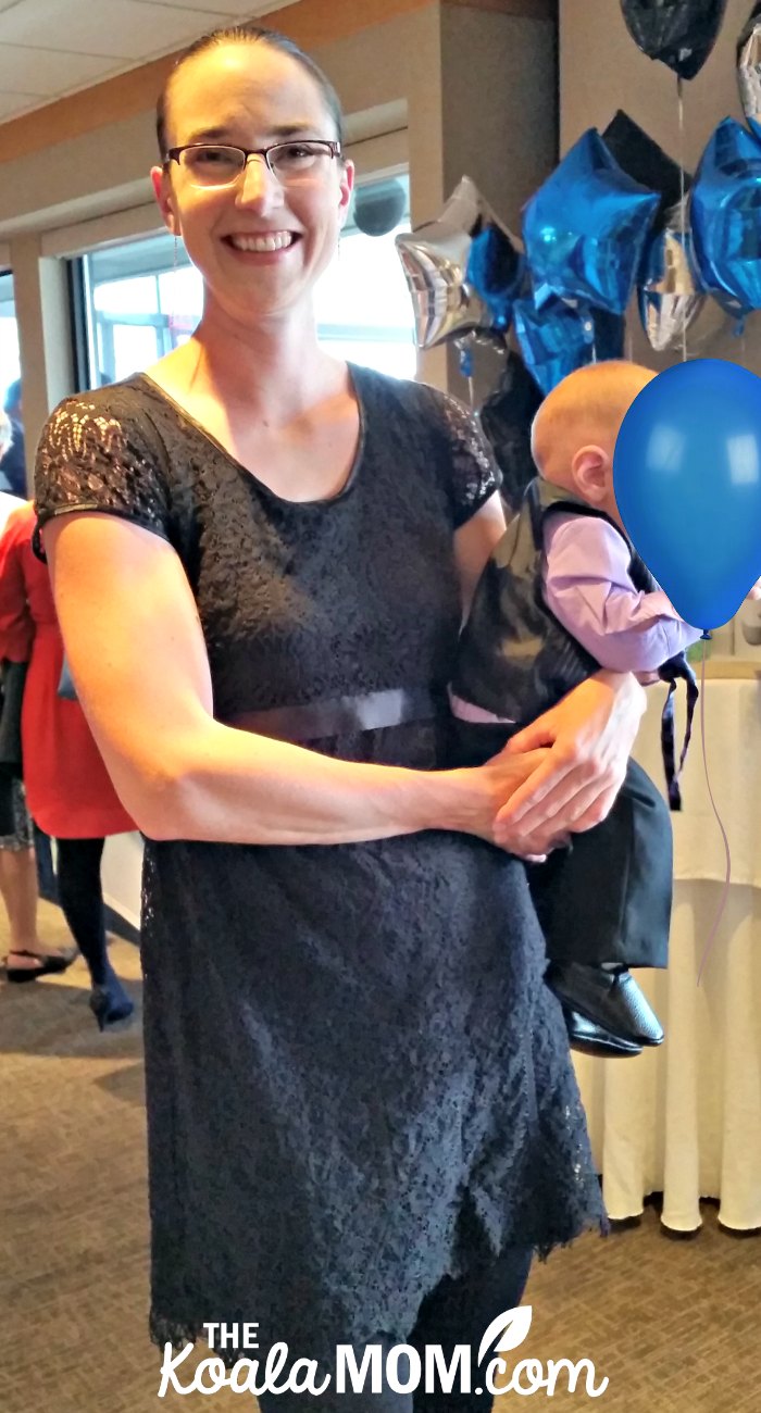 Bonnie wearing her black Momzelle nursing dress while holding her baby at a formal event.