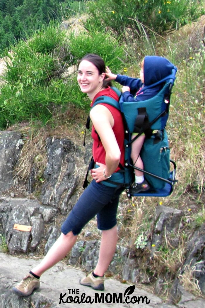 Mom carrying her toddler in a frame baby carrier.