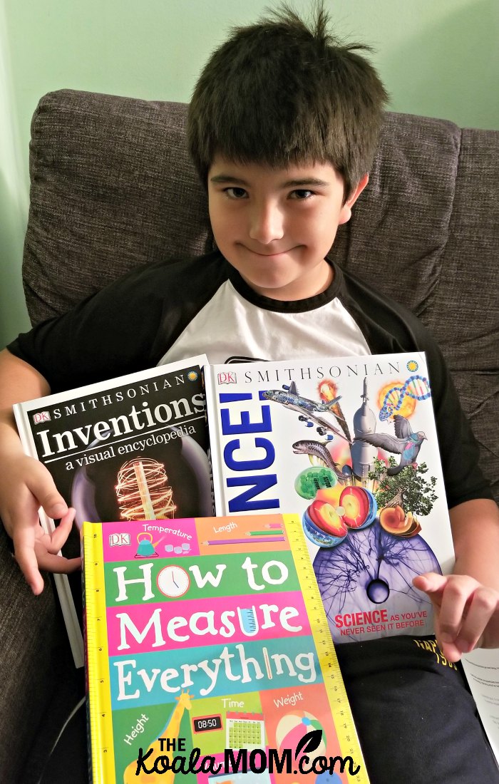 Boy holding three DK books that make science exciting - How to Measure Everything, Inventions: a Visual and Encyclopedia, and Discover Science!