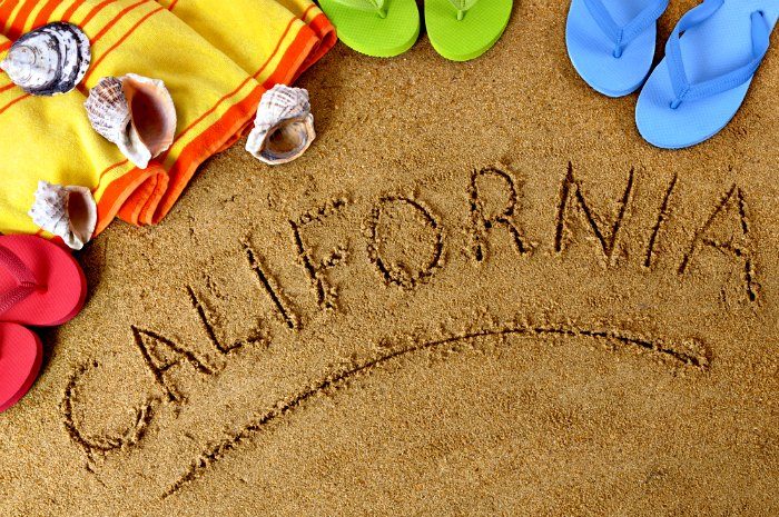 Beach background with towel and flip flops and the word California written in sand (studio shot - directional light and warm color are intentional).