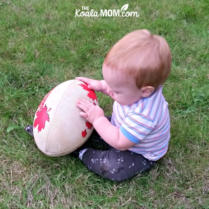 Baby boy holding a rugby ball (encourage your kids to play sports from a young age!)