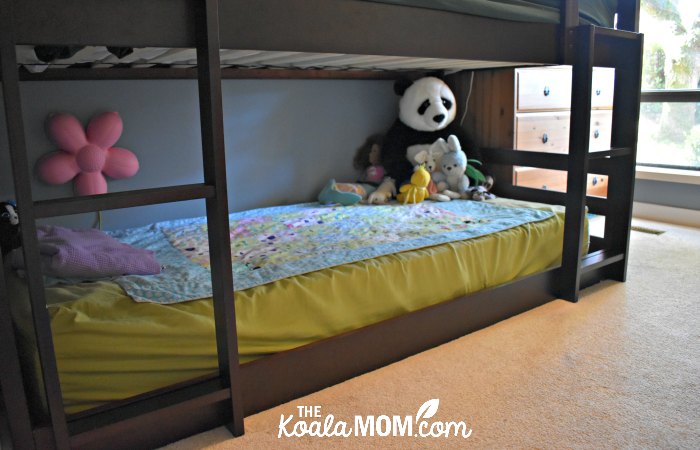 Stuffies and blanket on the mattress of the bottom bunk in a triple bunk bed.