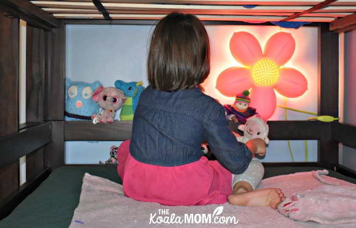 Girl playing with her stuffies in the middle bunk of a triple bunkbed.