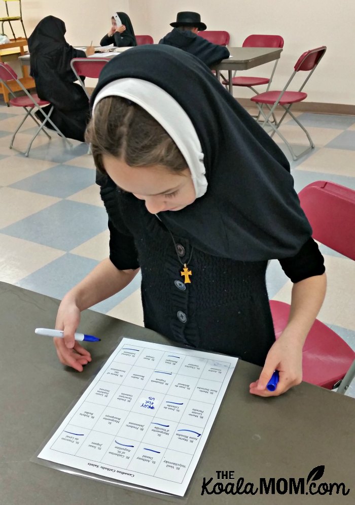 Girl dressed as a nun playing Canadian saint bingo at our Canadian All Saints Day Party.