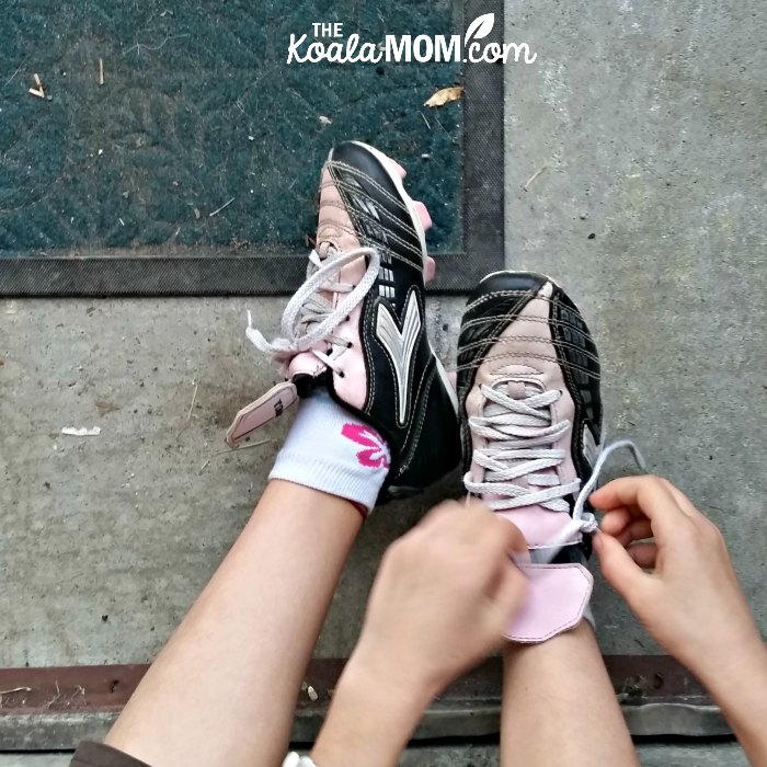 8-year-old girl tying up her pink cleats before a mini rugby practice (cool shoes could help encourage your kids to play sports)