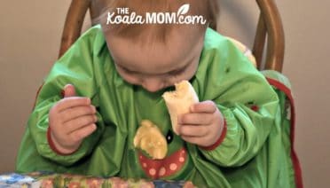 Baby feeding himself banana while wearing a Bibado bib.