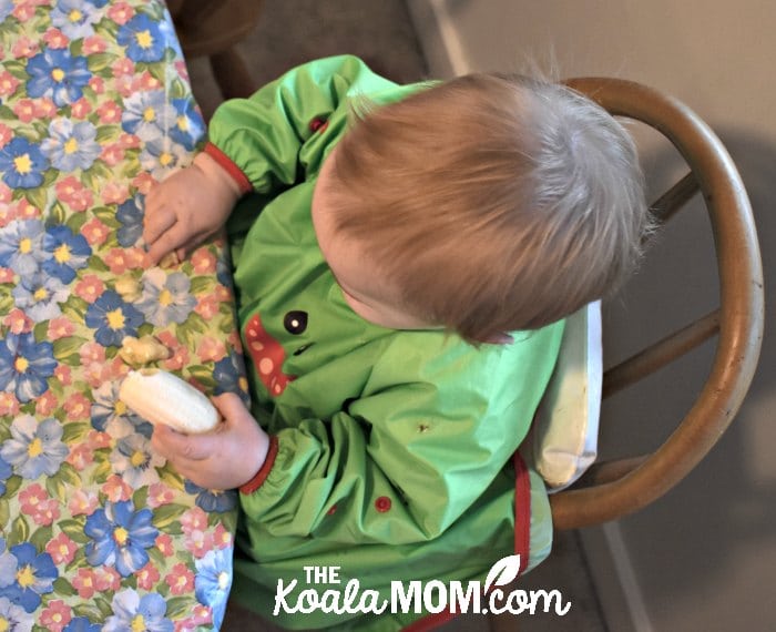 Baby eating a banana while wearing a green Bibado baby bib. 