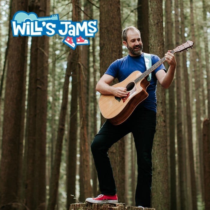 Will Stroet playing his guitar on a tree stump in the forest.