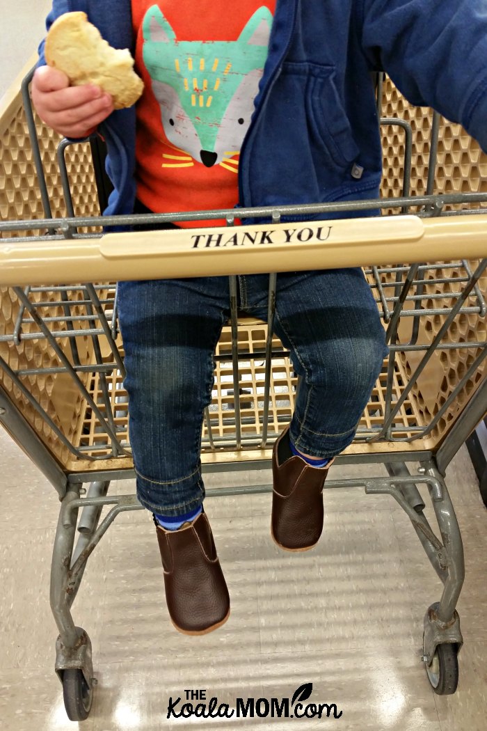 Baby sitting in a grocery cart, eating a sugar cookie from the bakery.