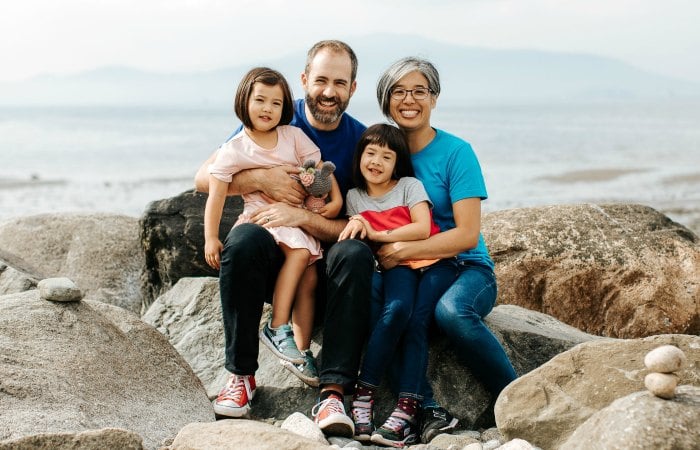 Kim The, Will Stroet, and their daughters posing on a beach.