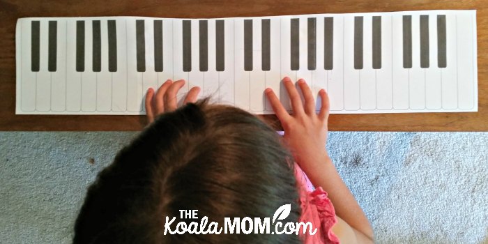 6-year-old pretending to practice piano on her paper keyboard.