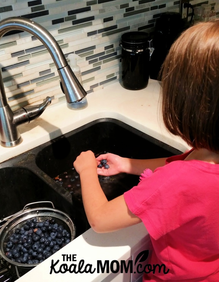 Child washing fresh berries in a sink.