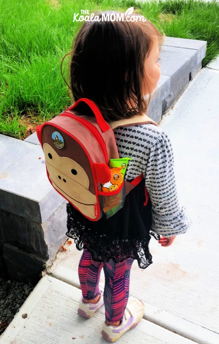 Toddler wearing a monkey backpack with FreeYumm snacks tucked in the pocket.