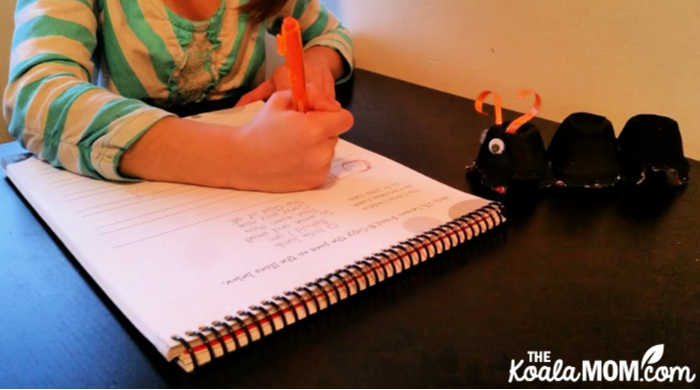 Grade 1 student doing handwriting with her egg carton ant watching.