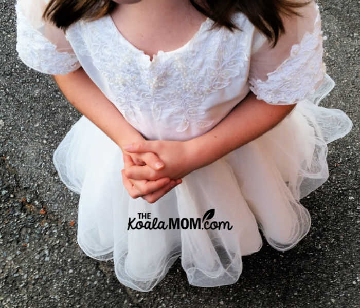 Girl wearing her First Communion dress with folded hands.