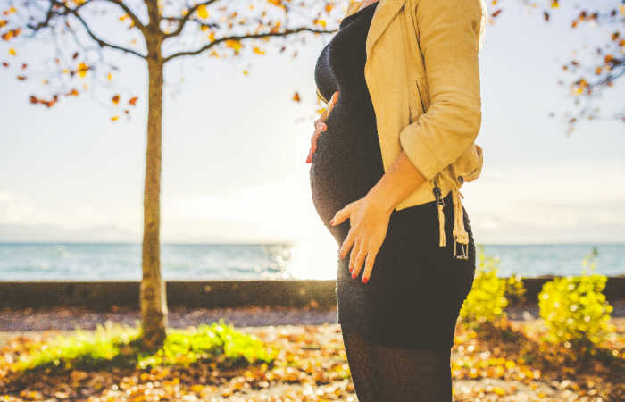 Postpartum woman wearing a black dress and a beige jacket.