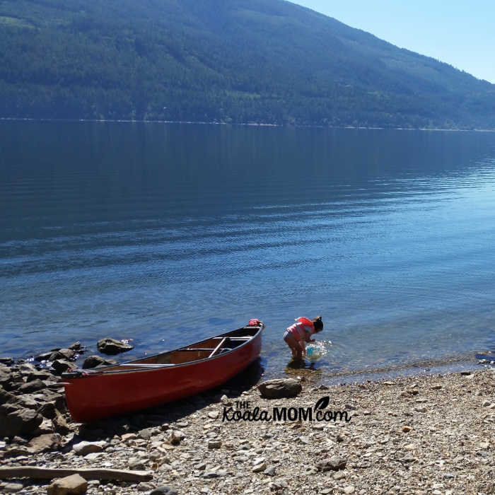 4-year-old plays in lake near a beached canoe.