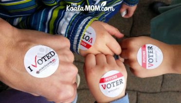 Mom and three kids with "I voted" / "Future voter" stickers on their hands.