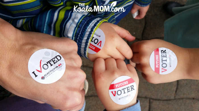 Mom and three kids with "I voted" / "Future voter" stickers on their hands.