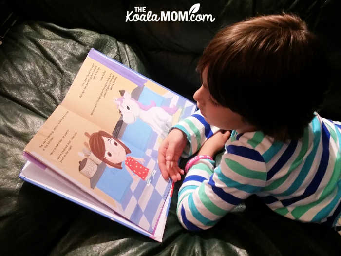 7-year-old girl laying on her stomach on a couch, reading her Me & My Pet book.